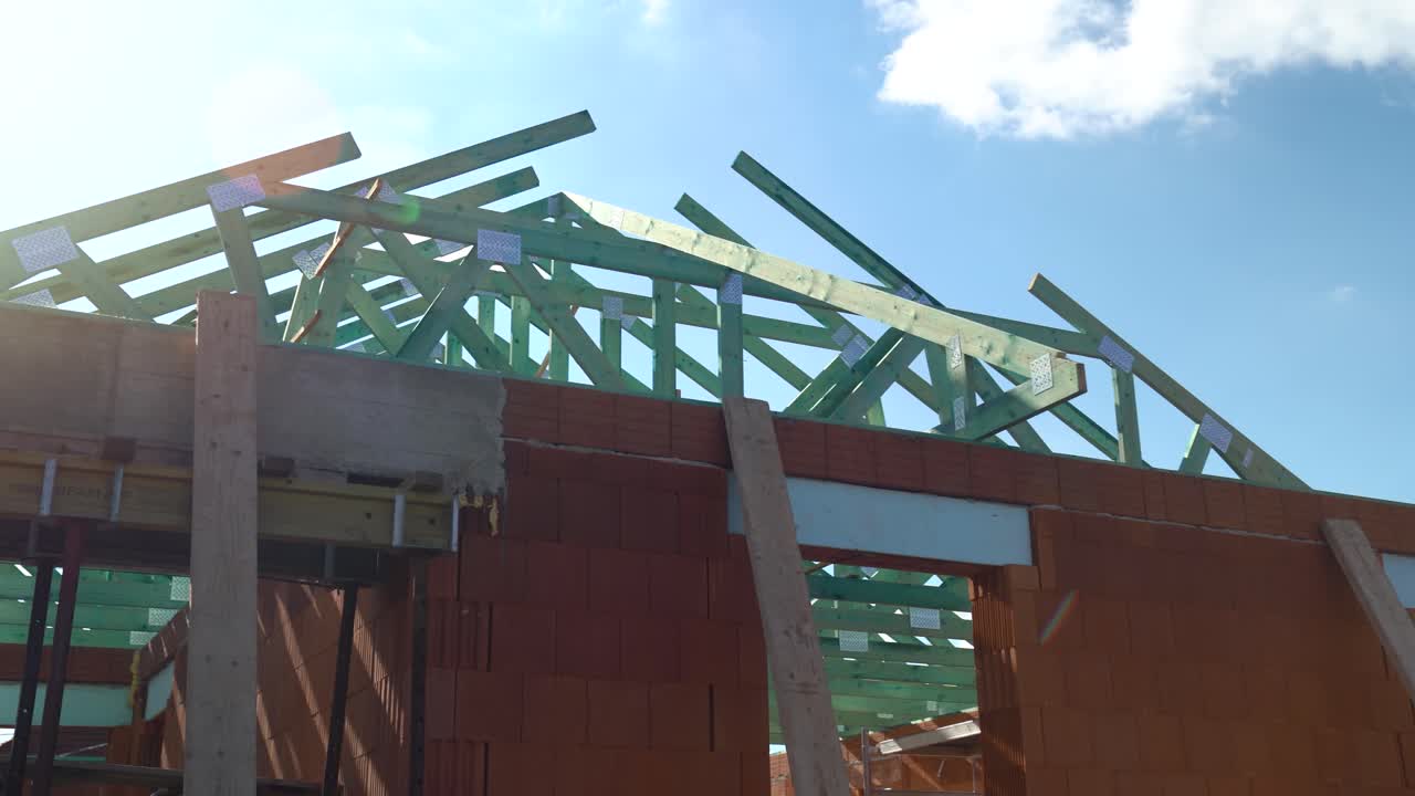Timber trusses on brick house roof under bright sky with scaffolding, hadheld shot