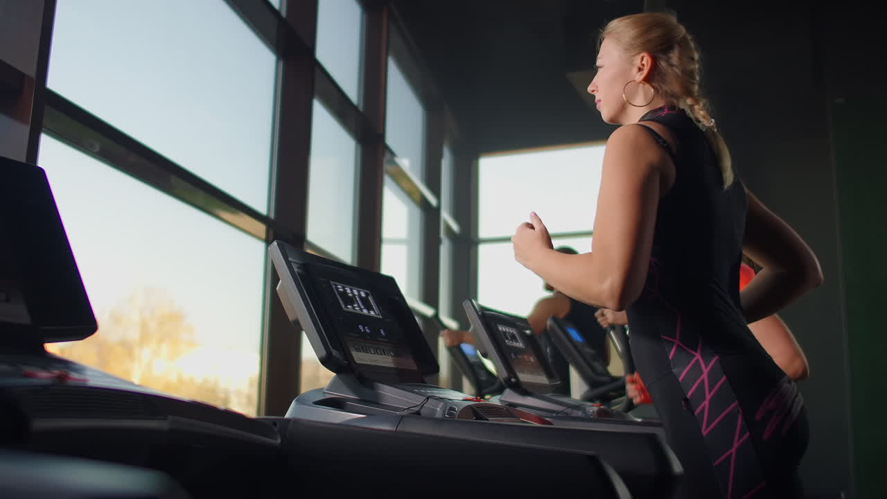 Cute young girl running on a treadmill in front of panoramic Windows in the fitness room. Gym with treadmill and large Windows.