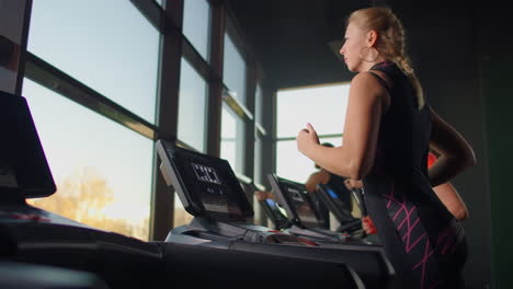 cute young girl running on a treadmill in front of panoramic windows in the fitness room. gym with treadmill and large windows.