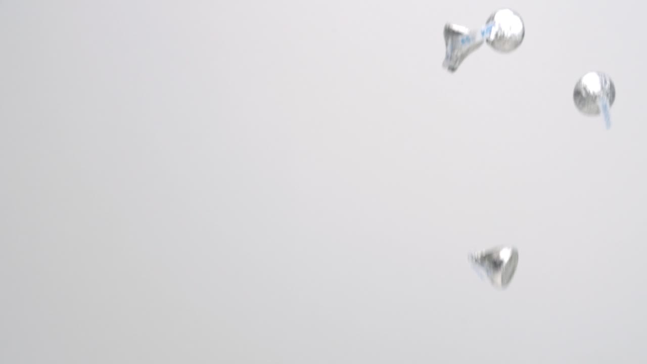 шоколадные конфеты hershey's kiss в серебряной обертке падают дождем на белый фон в замедленной съемке