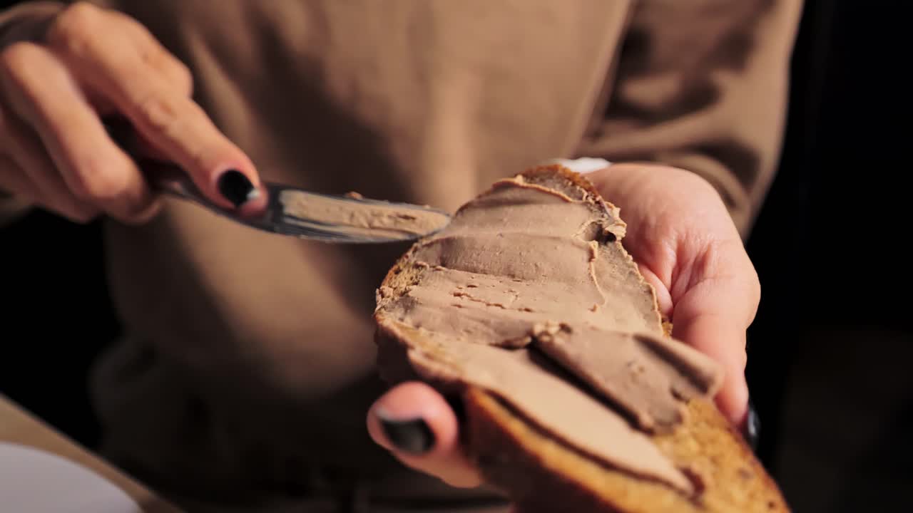 Close view of pâté routine as hand gently spreads rich meat paste on brown slice