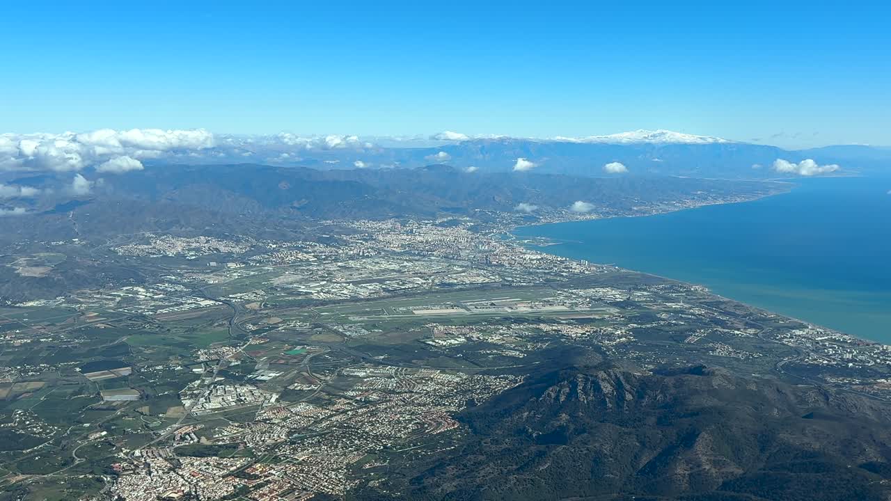 Una vista elevata dalla cabina di pilotaggio della città di Malaga, dell'aeroporto e del porto, con la Sierra Nevada innevata sullo sfondo in una soleggiata giornata invernale