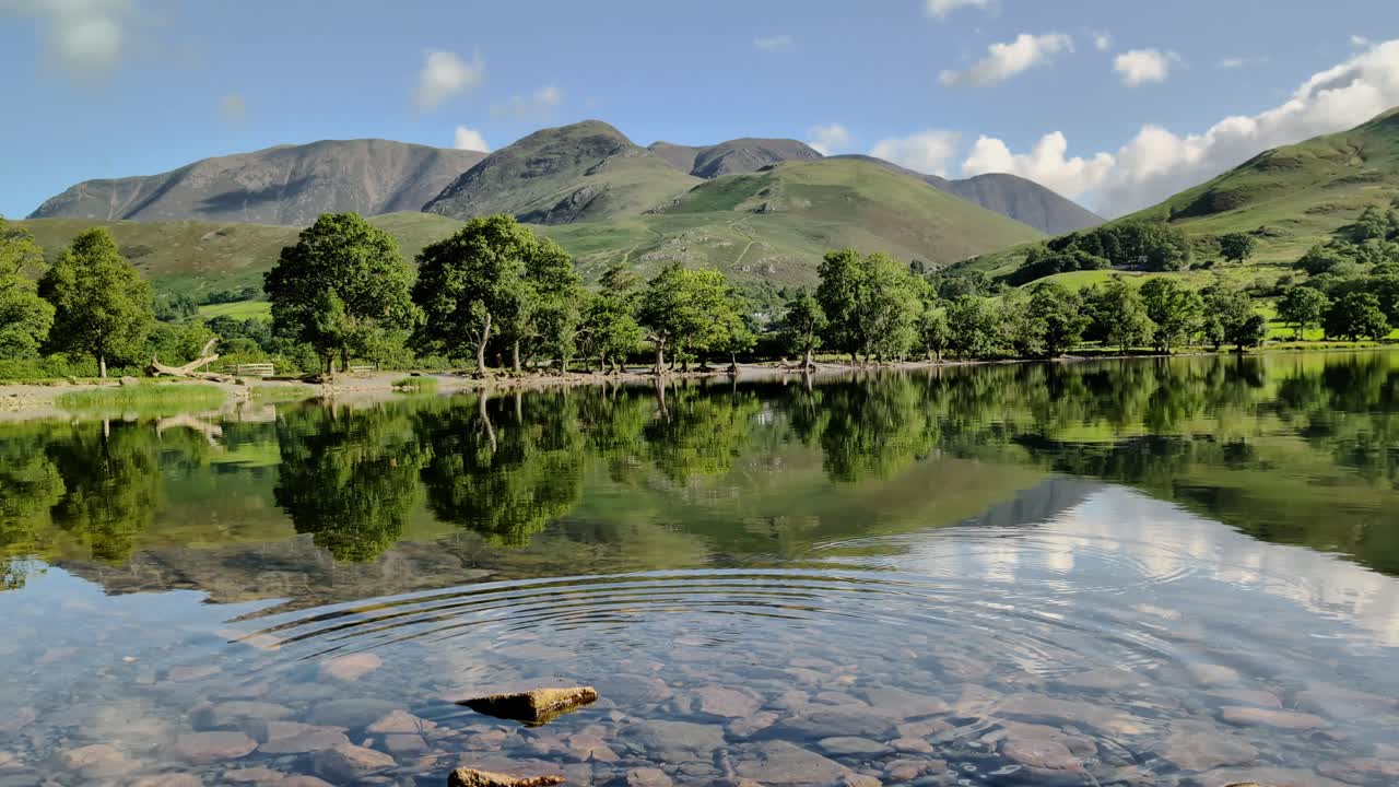 view of Buttermere Lake on a bright, sunny day. The calm water reflects the Lake District fells