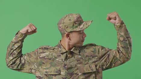 close up of asian man soldier smiling and flexing his bicep while standing in the green screen background studio