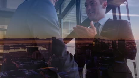 Digital-composition-of-two-caucasian-businessmen-shaking-hands-at-office-against-night-cityscape