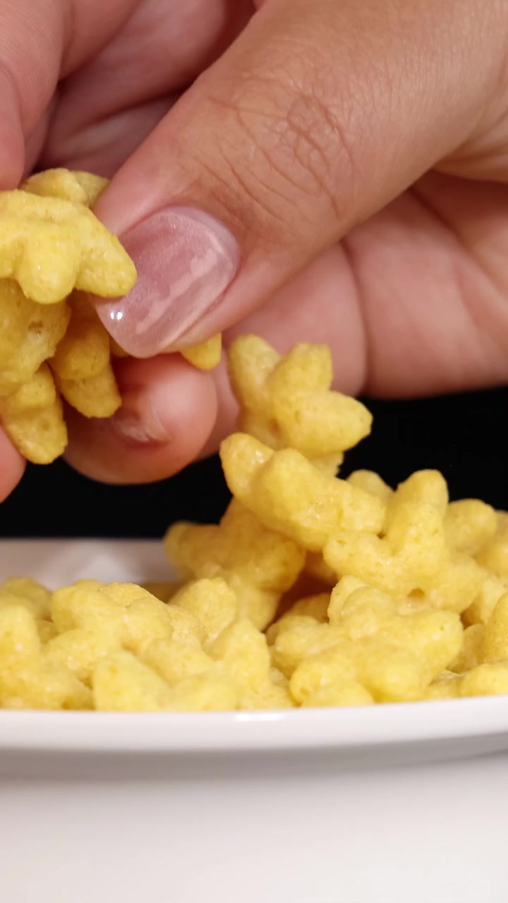Una mano seleziona pezzi di cereali a forma di stella da una ciotola su uno sfondo nero, in primi piani.