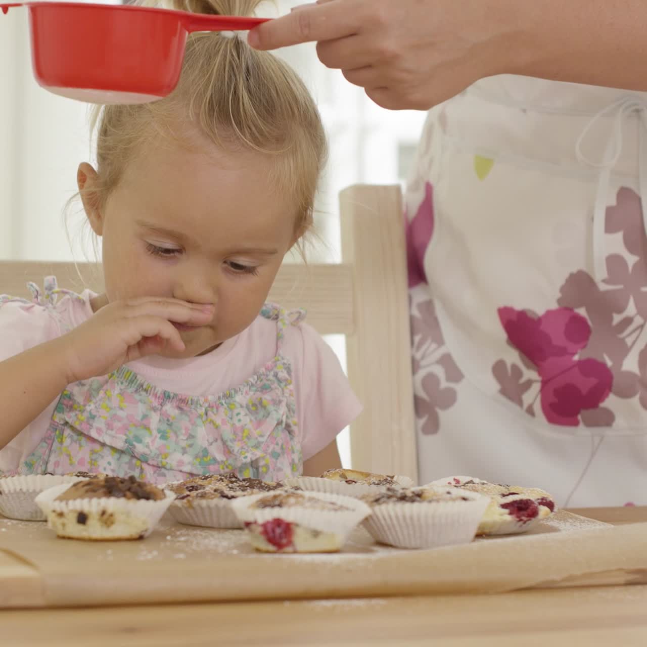 chica viendo caer azúcar en muffins horneados