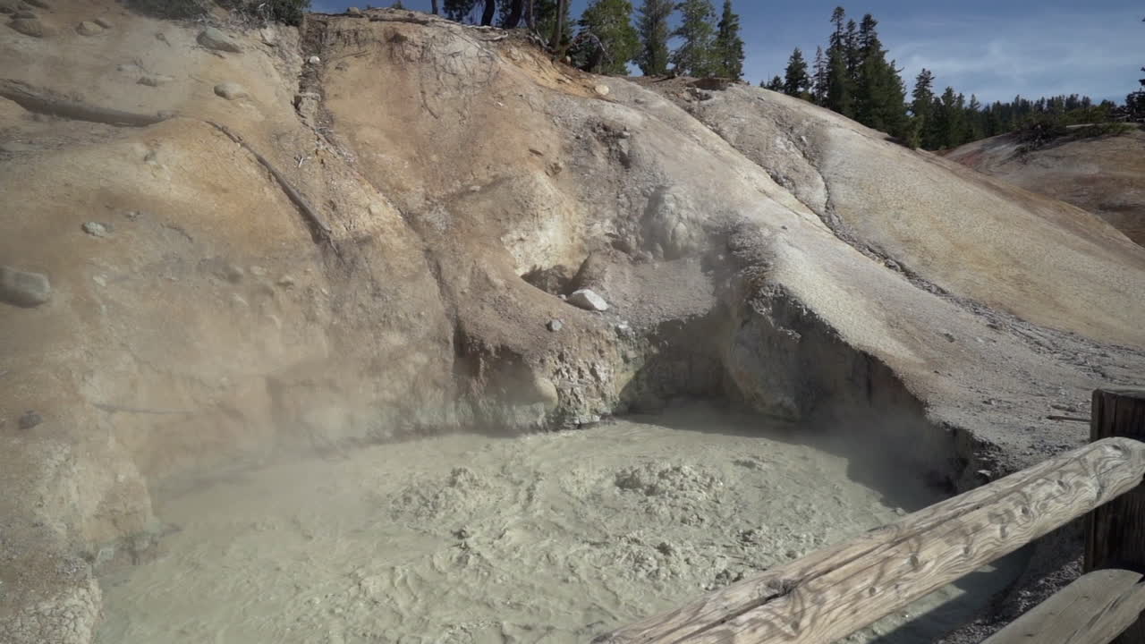 Slow motion of a boiling muddpot at Lassen Volcanic National Park and a wooden fence in the foreground