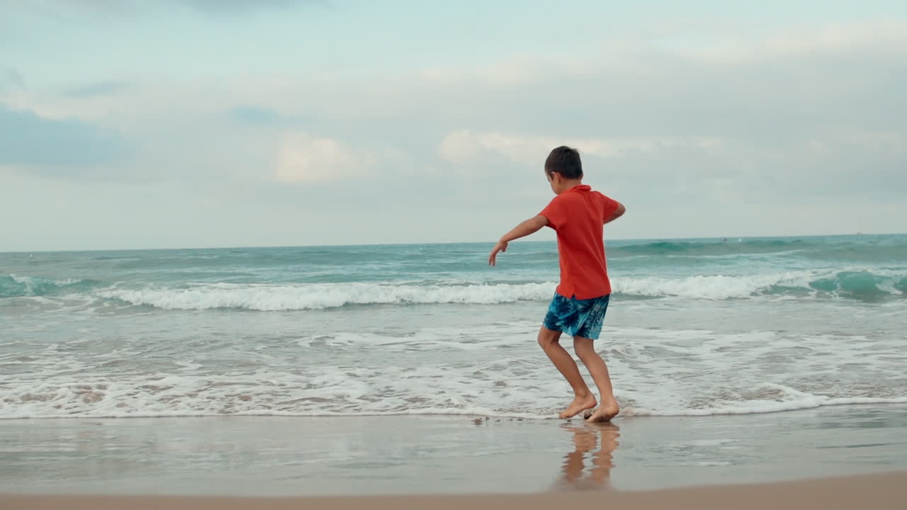 Happy boy dancing at sand beach in holiday. Active guy having fun at sea surf.