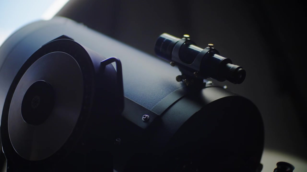 Close up view of a small finderscope mounted on the main optical tube of a large professional astronomical telescope inside a dark observatory