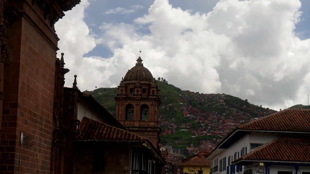 Capela de Nossa Senhora de Loreto em Cusco, Peru, com campanário colonial acima dos telhados da cidade velha e encosta verde dos Andes sob nuvens dramáticas