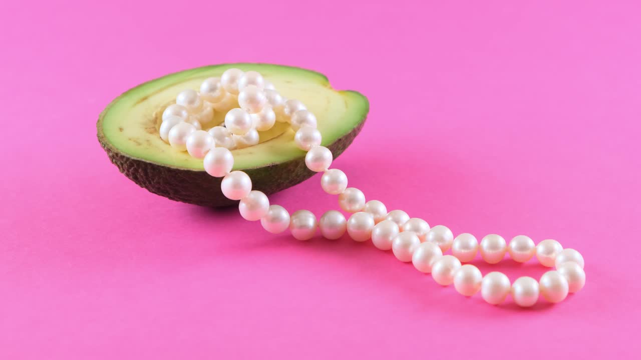 полусвежий плод авокадо с жемчугом на розовом фоне. модный дизайн еды