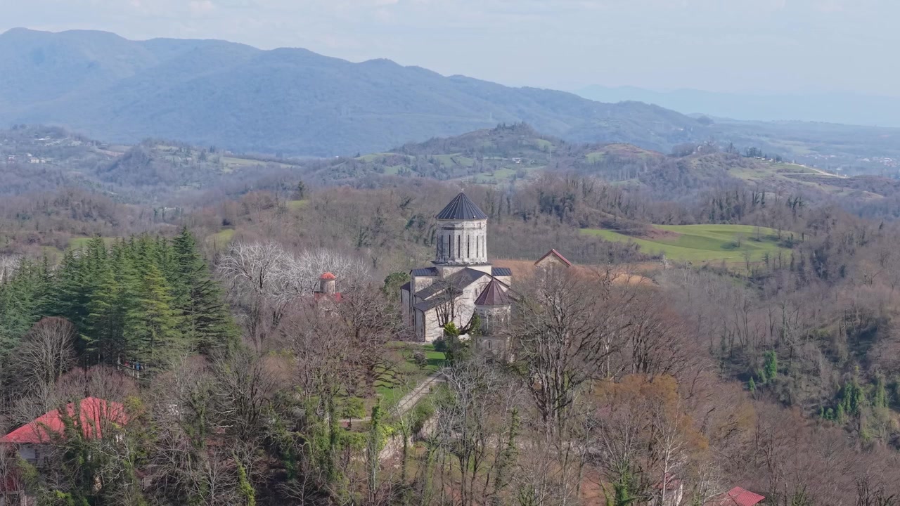 Drone shot capturing Martvili Monastery perched on a hilltop, rising above deciduous trees during early spring and surrounded by the peaceful landscape of western Georgia.