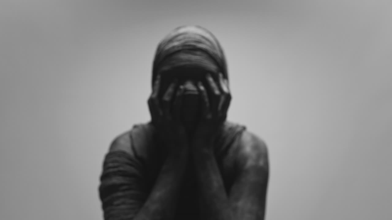 A mummified woman against the bright background in keeps her hands on her face the powerful pose full of despair