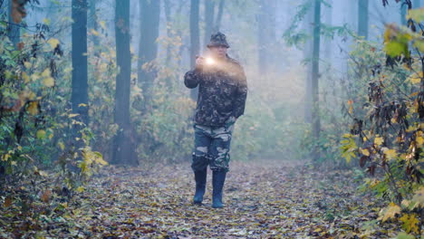 un hombre camuflado camina por el bosque iluminando su camino en la niebla buscando a los desaparecidos