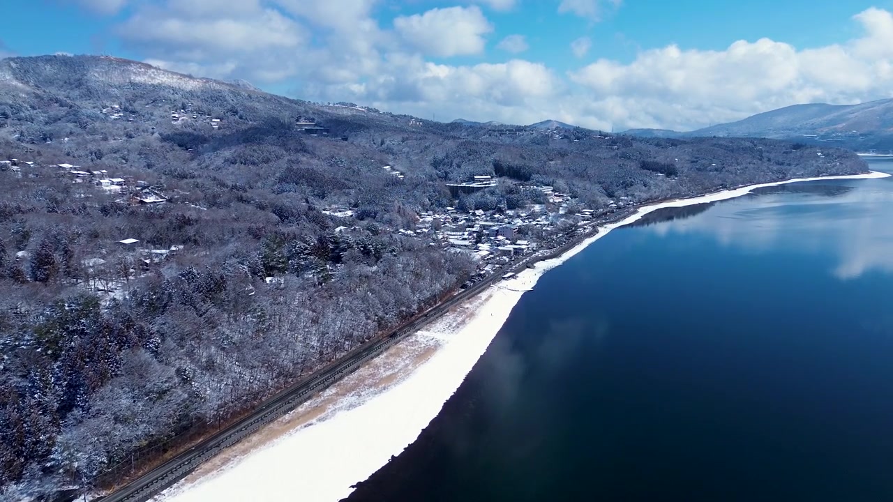 Phong cảnh từ trên không bằng drone của vùng ngoại ô thị trấn Yamanakako với cây rừng phủ tuyết và một con đường chính bên cạnh các tuyến đường thủy hồ trong thung lũng của Quận Minamitsuru, gần Núi Phú Sĩ, Nhật Bản. Cảnh quan du lịch ngoài trời ở châu Á.