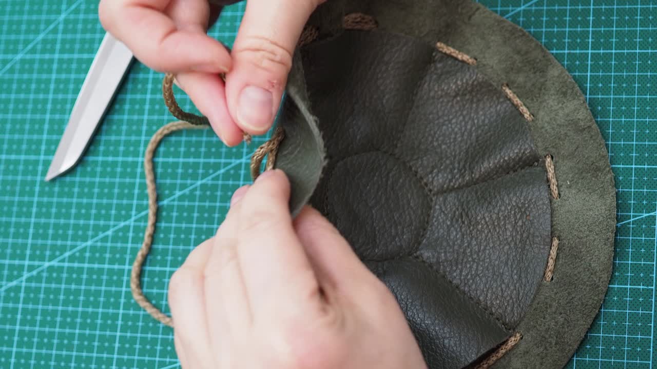 el artesano inserta un cordón en la bolsa cosida