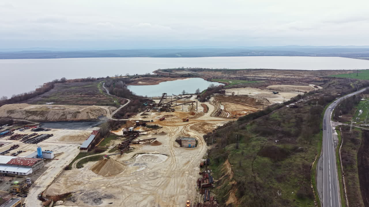 Construction site near water with heavy machinery and vehicles working on land development in a rural area during cloudy weather