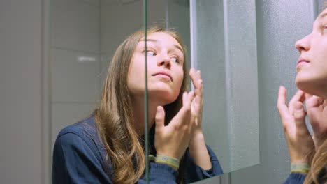 Attractive-young-woman-taking-care-of-face-skin-against-mirror,-close-up