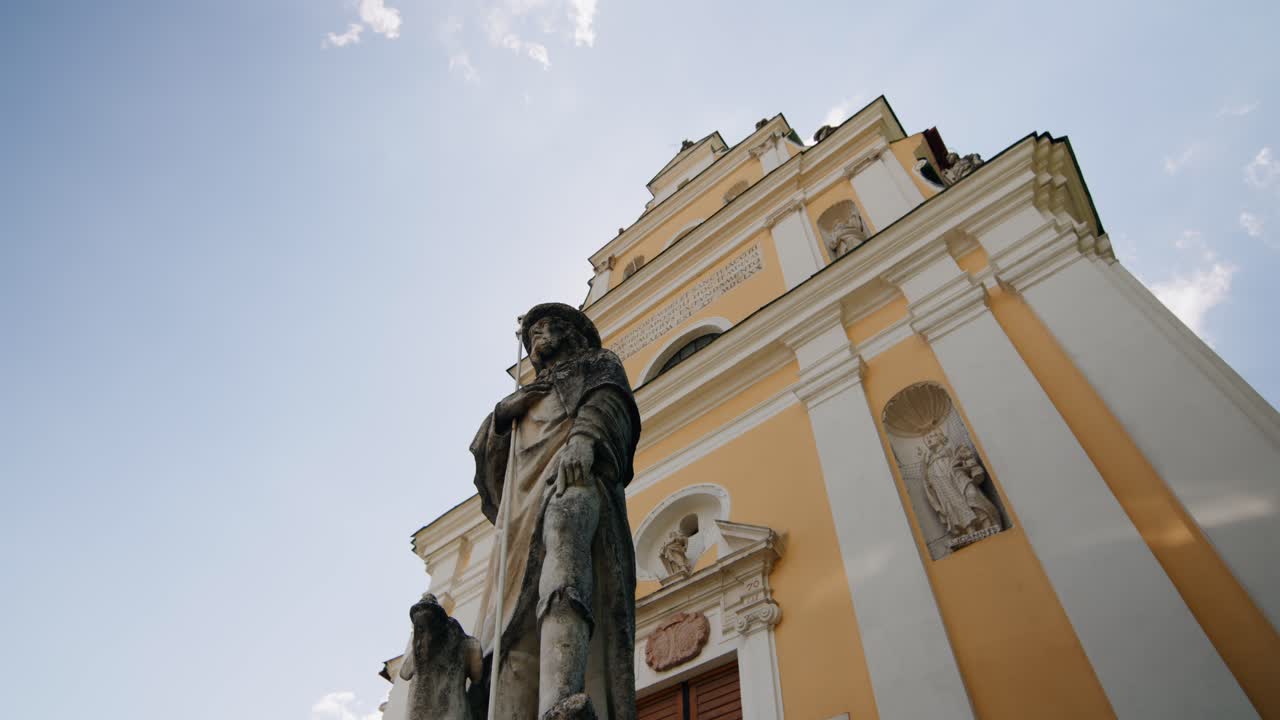 panorámica alrededor de una estatua de piedra frente a una antigua iglesia católica en falkenstein, austria en un día soleado de verano