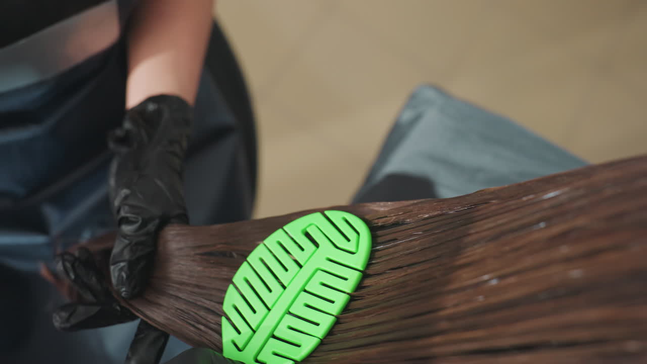 윤기 있는 갈색 머리카락을 섬세하게 풀고, 촘촘한 빗으로 매끄러운 머리카락을 조심스럽게 빗어 분리하는 모습을 클로즈업하여 보여주는 장면이에요. 윤기 있는 갈색 머리카락을 섬세하게 풀어주는 정확한 장면을 포착했습니다.