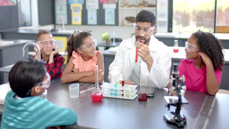 in a school classroom, a biracial male teacher demonstrates a science experiment