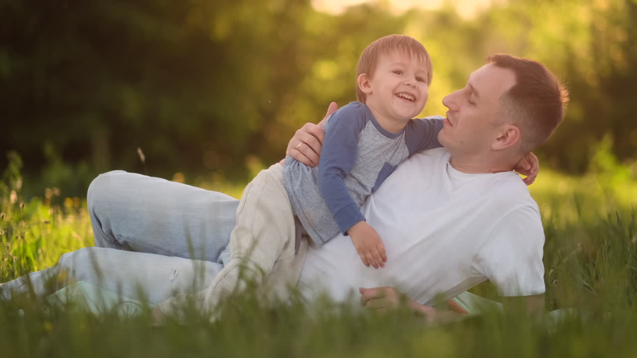 Padre e figlio affettuosi che si abbracciano sull'erba al tramonto al rallentatore