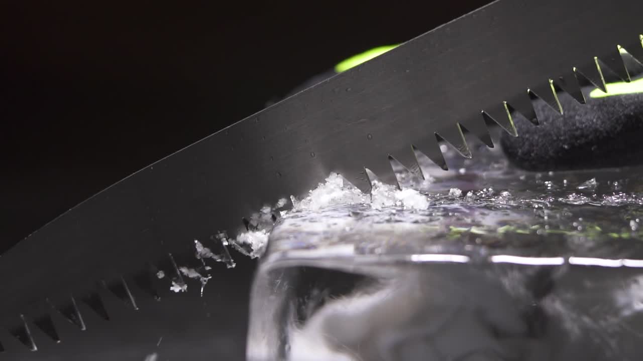 A bartender is cutting the ice block to smaller pieces for cocktail service by using a long toothed knife.