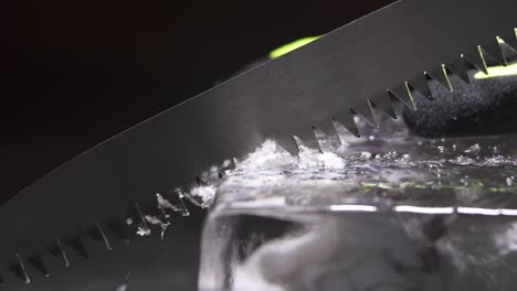 a bartender is cutting the ice block to smaller pieces for cocktail service by using a long toothed knife.