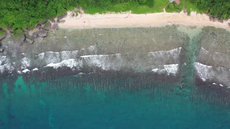 Tiro-De-Seguimiento-Aéreo-De-Arriba-Hacia-Abajo-Que-Captura-El-Arrecife-Bordeante-De-Houshi-Y-El-Hermoso-Agua-De-Mar-Turquesa-Con-Olas-Rompiendo-La-Costa-En-La-Cueva-Enana-Negra-En-La-Isla-Xiaoliuqiu-Lambai,-Taiwán