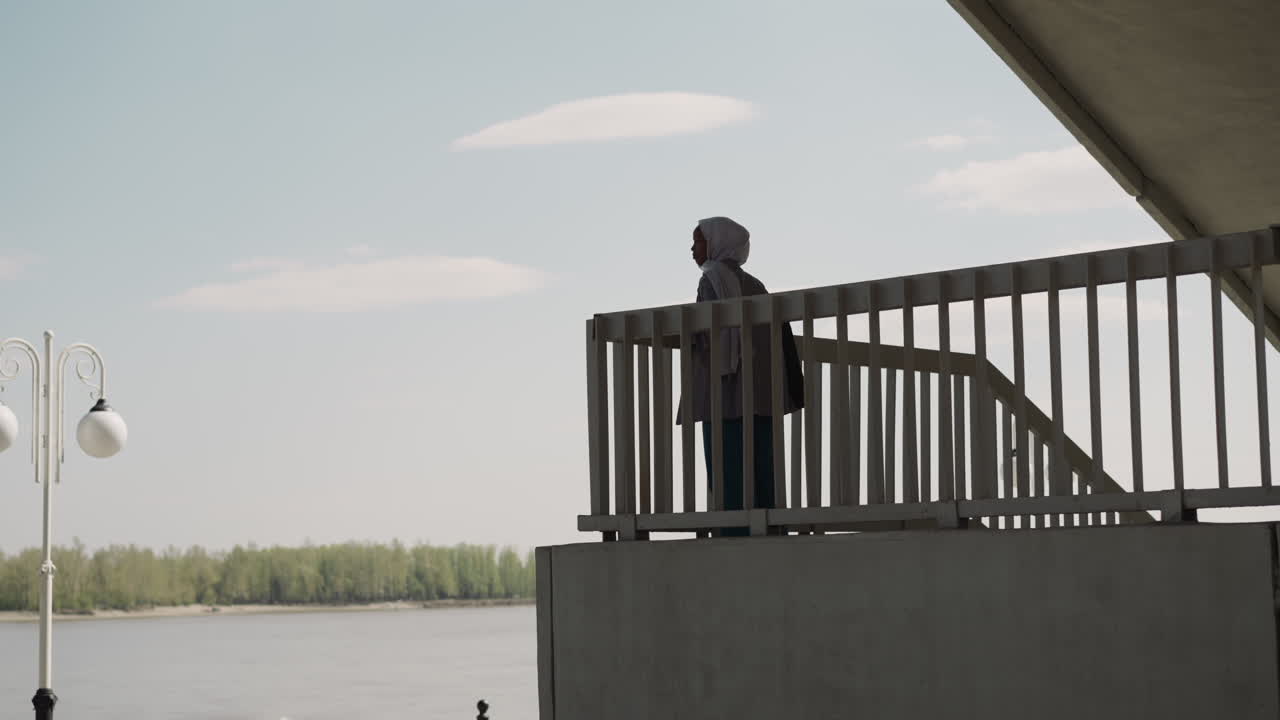히자브 를 입은 흑인 여자 가 다리 아래 의 강 을 바라보는 장면 을 즐긴다
