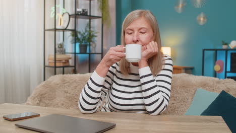 mature woman happily closing laptop after completing important task smiling and relaxing at table