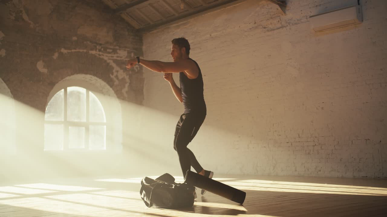 un hombre en un uniforme deportivo de verano negro está involucrado en la aptitud y la práctica de boxeo golpes en un gimnasio de ladrillo soleado