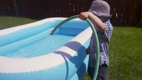 Süßer-Kleiner-Junge,-Der-An-Einem-Heißen,-Sonnigen-Tag-Seinen-Pool-Mit-Wasser-Füllt