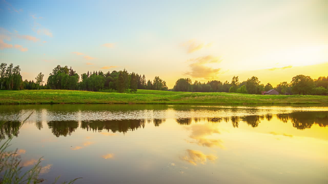 해가 지는 날 바람에 물이 움직이고 나무가 배경으로 움직이는 호수 위의 일몰의 영화적 타임  ⁇ 스