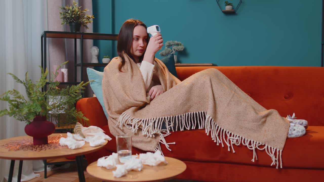 Young woman feels sick measuring body temperature with electronic thermometer at home coronavirus