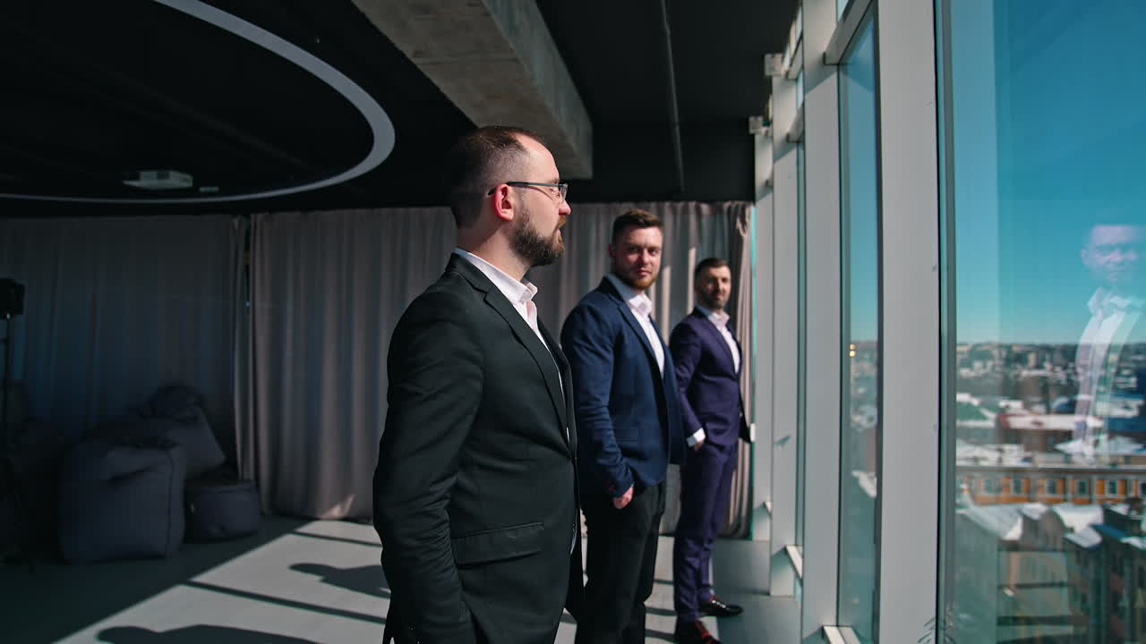 Serious business people in office. Three men in elegant suits looking at each other while standing at window and moving to the room.