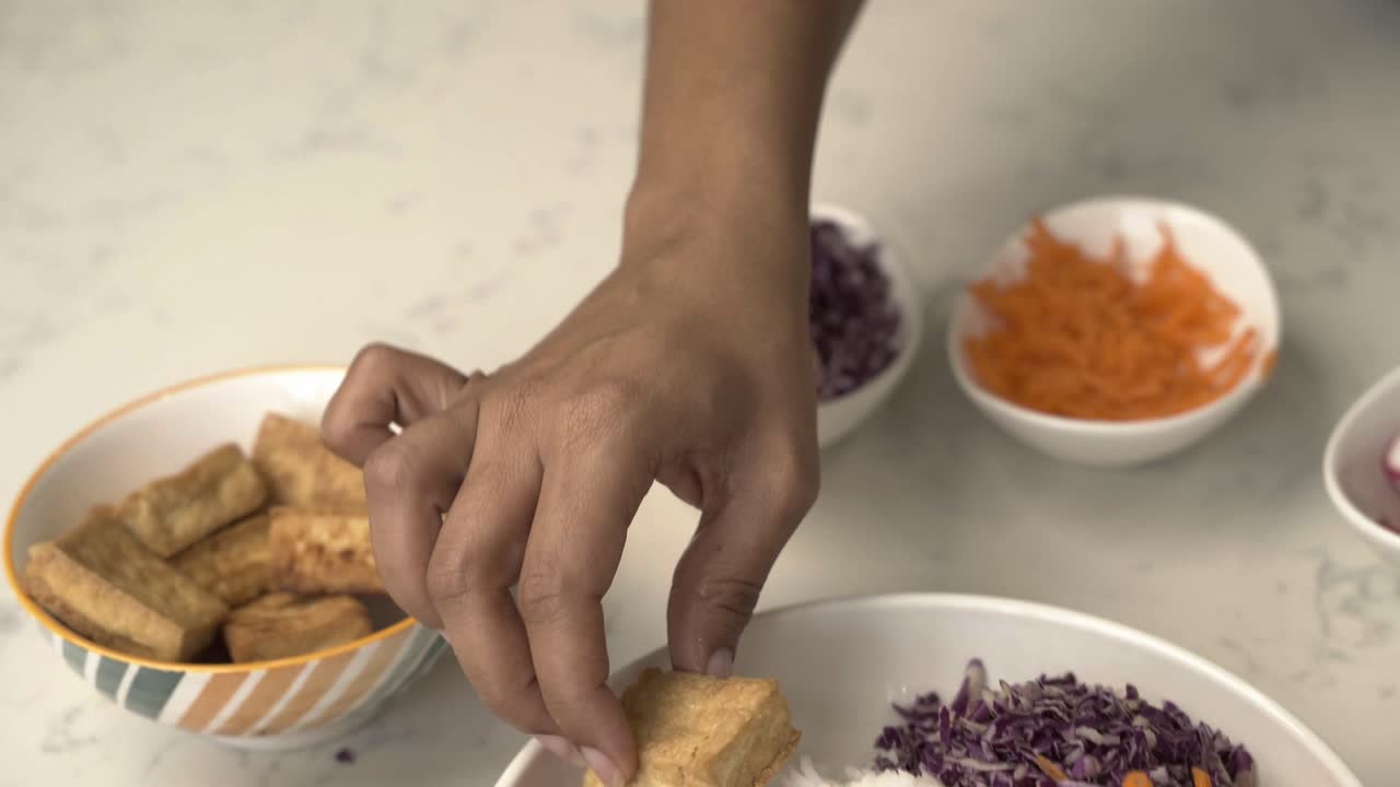 añadiendo tofu frito a un plato de tazón de fusión asiática con repollo rojo y zanahorias con un montón de arroz blanco