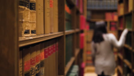 selective focus shot with sharp books in the foreground and a blurred background with a girl searching a book in the library, wondering around