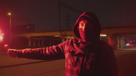 man in balaclava with red burning signal flare at night