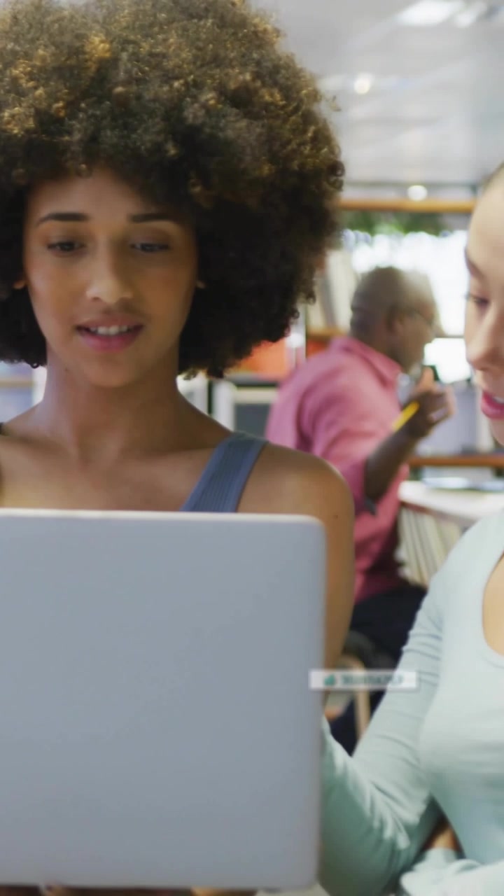 Video verticale: Donna che esamina un laptop mentre appaiono sovrapposizioni di identificazione, con un collega che si avvicina per una revisione tecnica.