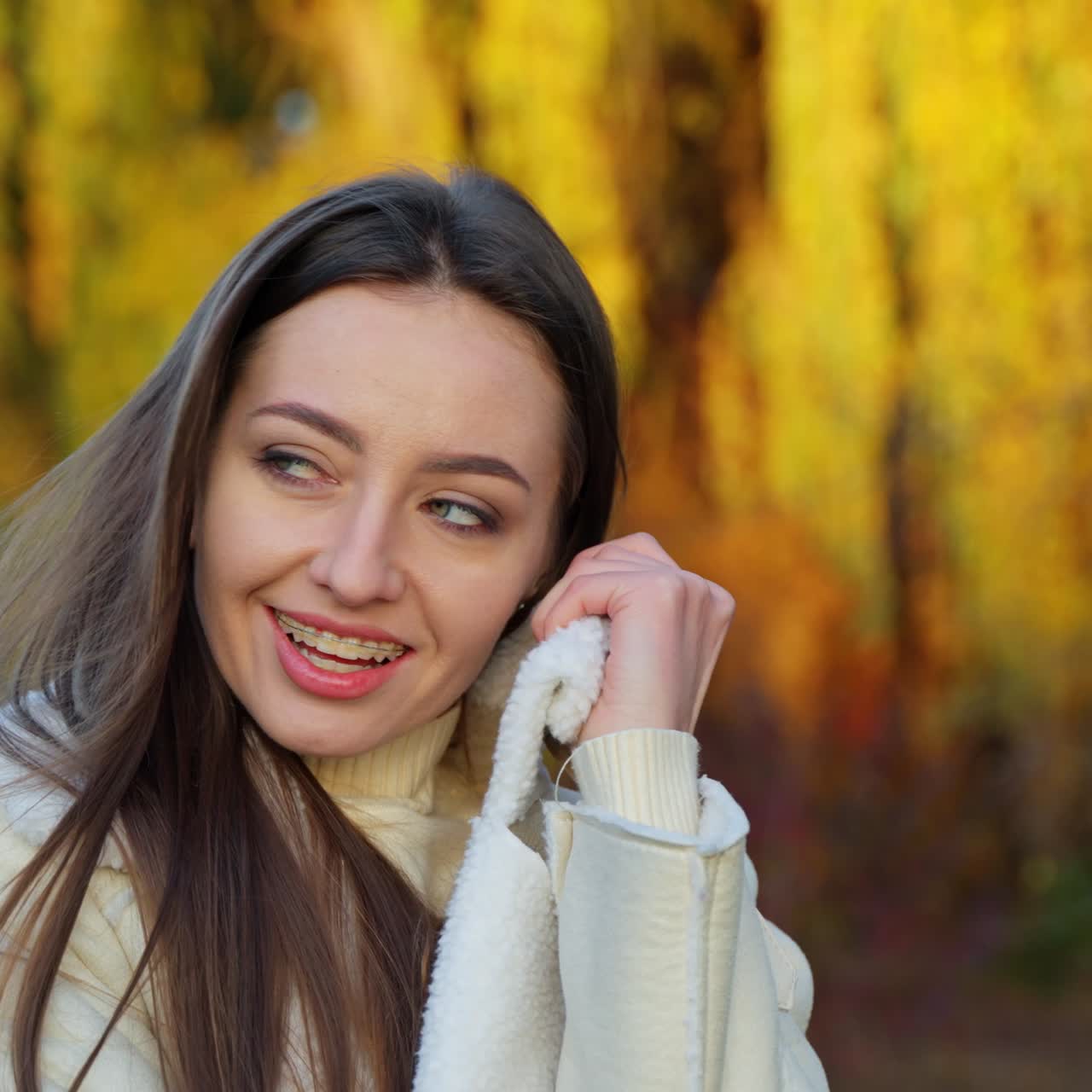 Happy brunette woman enjoying her time in the nature. Smiling lady wrapping herself up in jacket outdoors on autumn day. Blurred backdrop