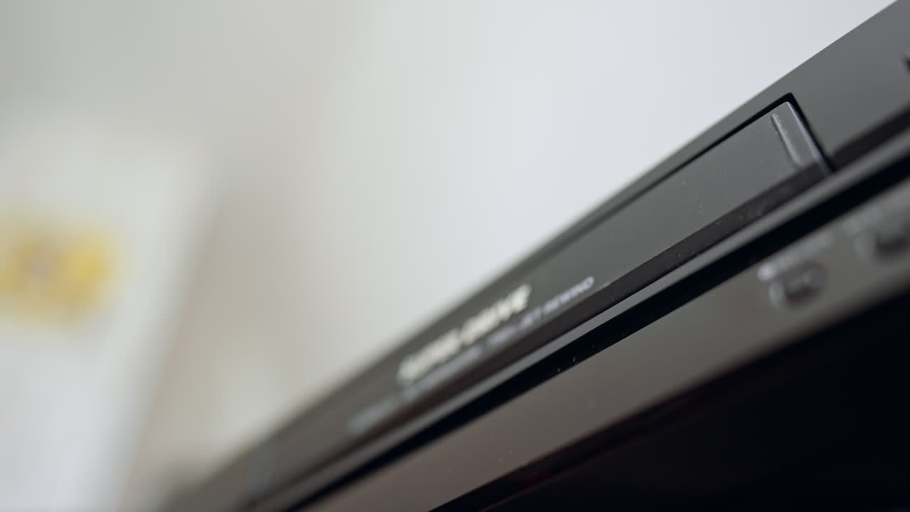 Black VHS cassette is put into the player. Low angle view. Extreme close up