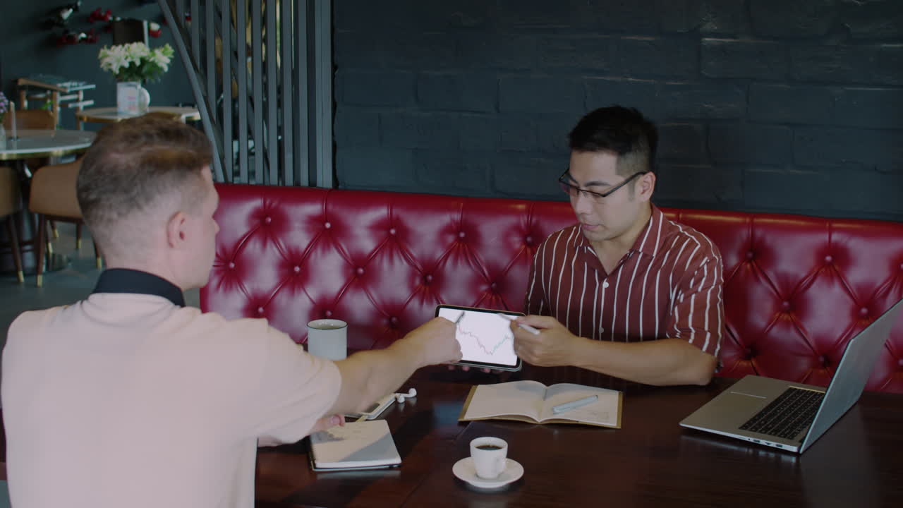 Young Trader Asking Expert about Stocks Forecast in Cafe