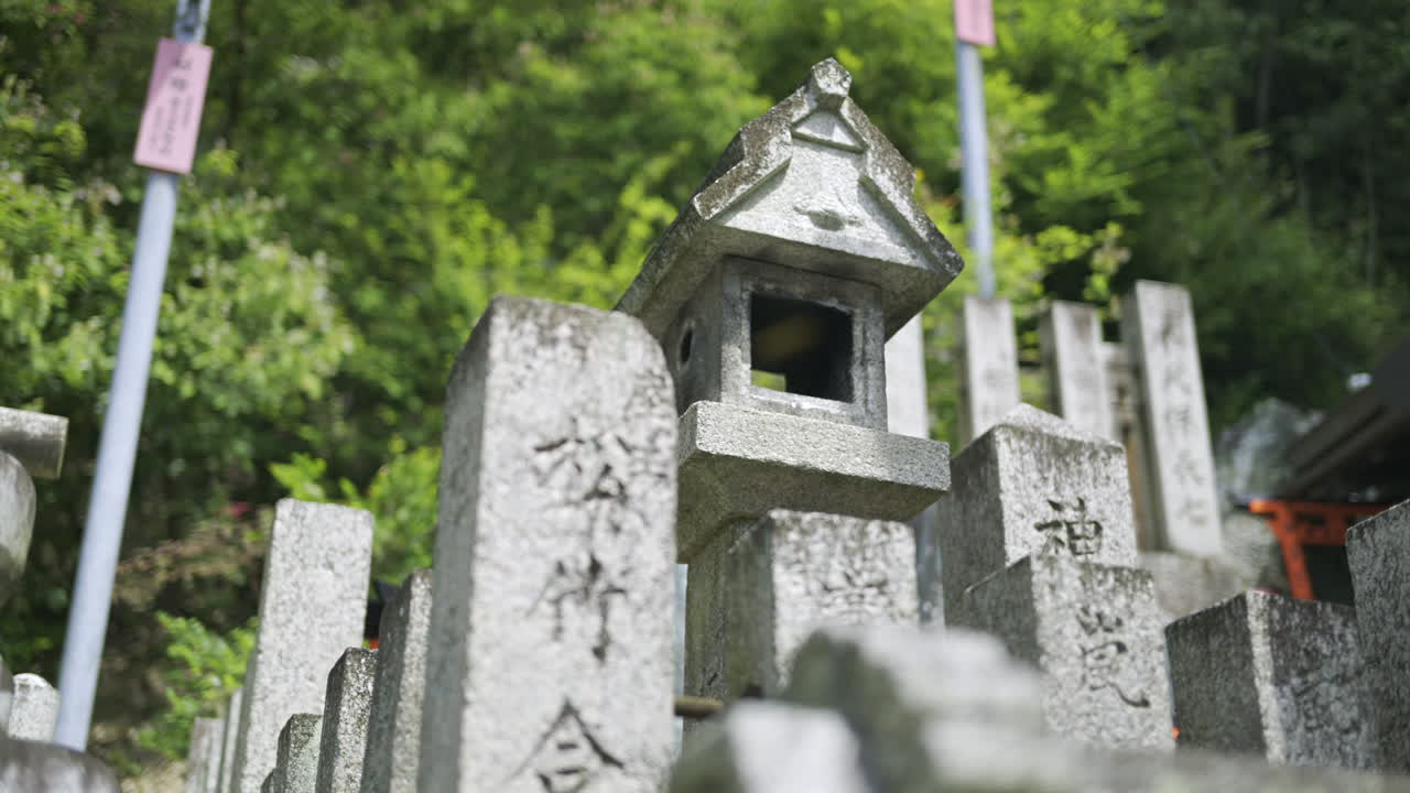 Many stone monuments with detailed inscriptions stand tall amid lush greenery in this tranquil forest area. Religious text in Japanese written on the stones. Kyoto, Japan, Fushimi Inari