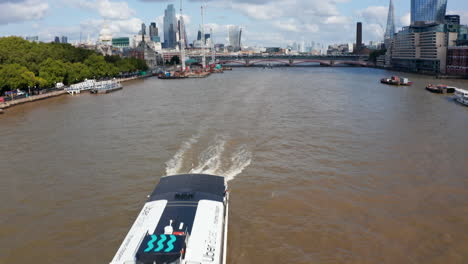 Boat-floating-against.-Tilt-up-reveal-of-embankments,-bridge-and-modern-buildings-in-background.-London,-UK