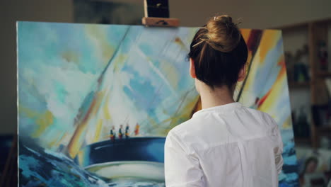 woman looking at abstract painting of sailing boats in an art studio