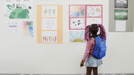 in school, young girl with backpack exploring colorful educational posters on wall