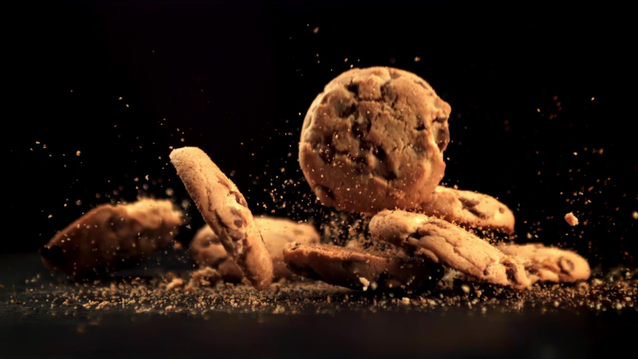Deliziosi biscotti con gocce di cioccolato che cadono e si sbriciolano su sfondo nero