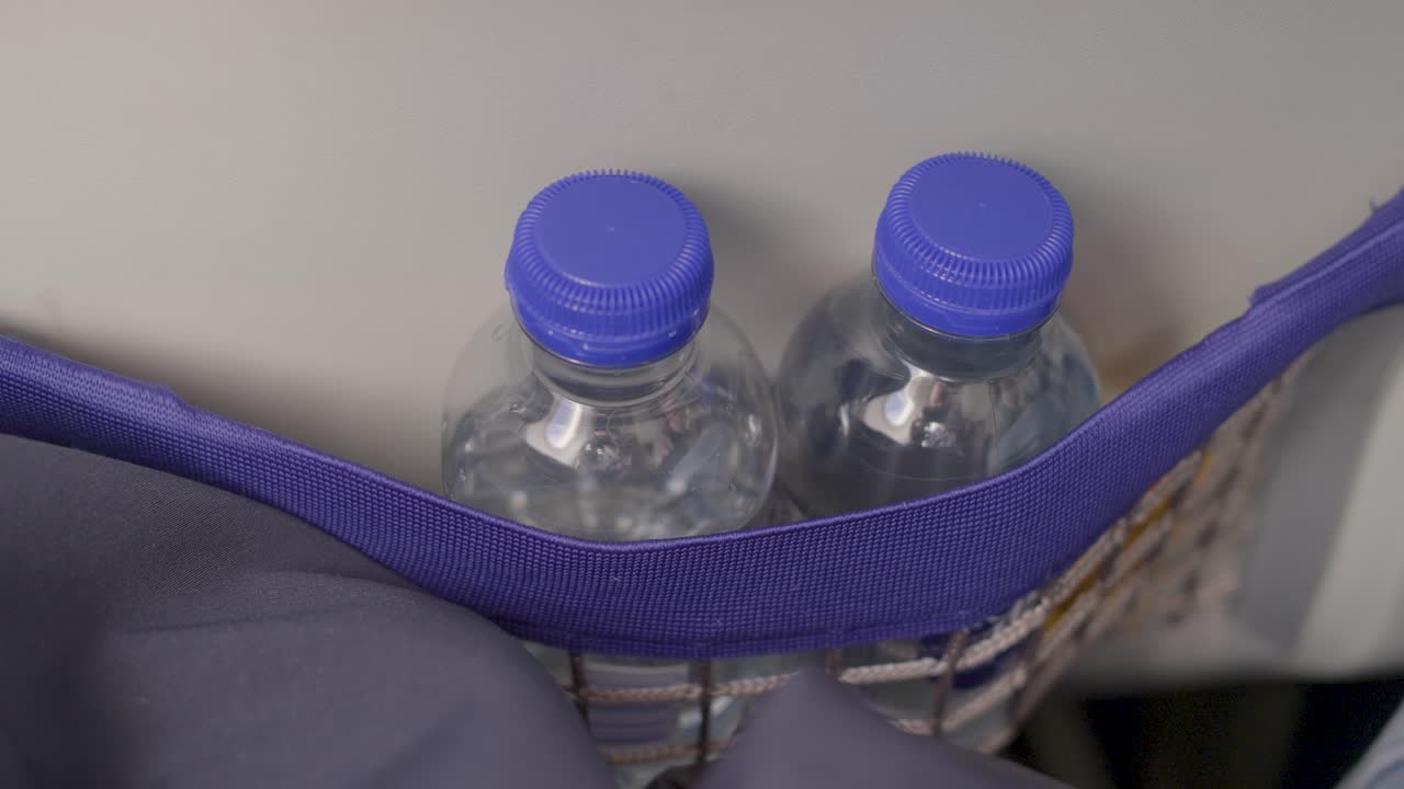 Two water bottles with blue caps in a seat pocket on a passenger plane